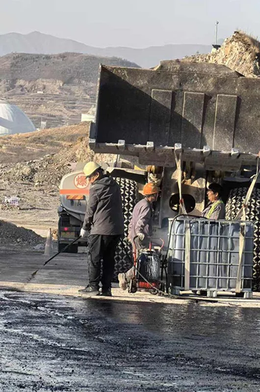 Road treatment crew with spraying equipment and an IBC tank at a mine