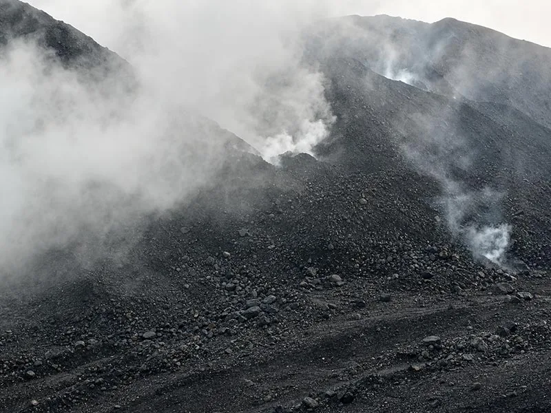 Dark bulk material stockpiles with white plumes above the surface