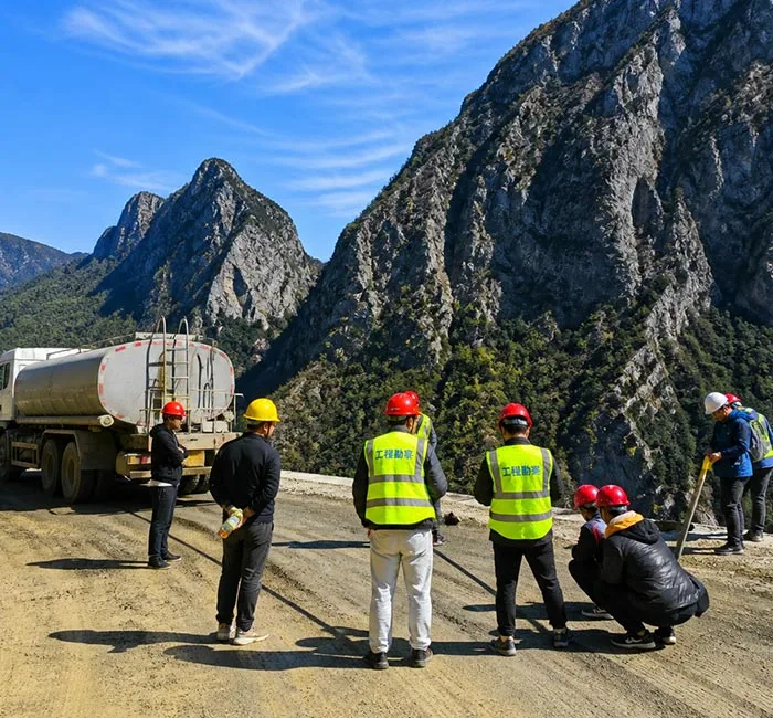 Workers inspecting an unpaved mountain road beside a tanker truck